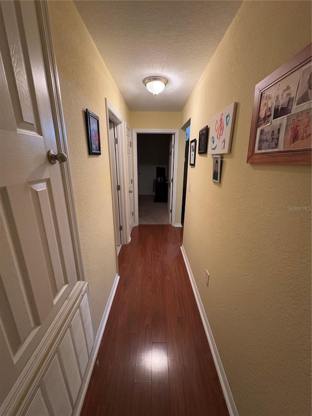 hallway with a textured ceiling and dark hardwood / wood-style flooring