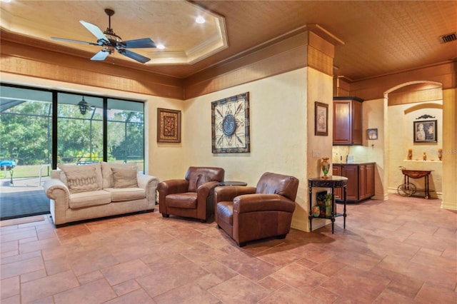 living room with a raised ceiling, ceiling fan, crown molding, and wood ceiling