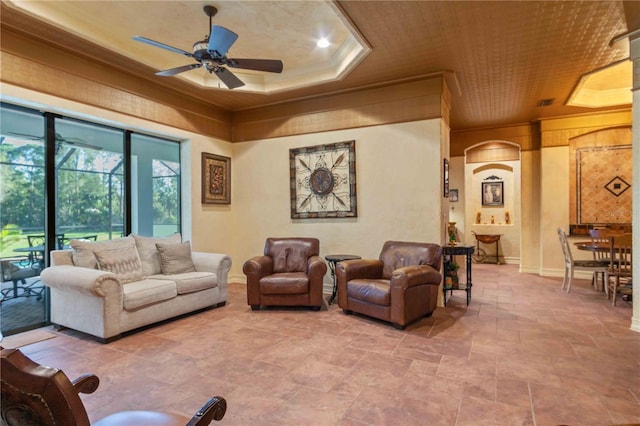 living room featuring a raised ceiling, ceiling fan, and crown molding