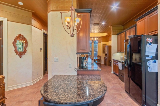 kitchen with dark stone counters, black refrigerator, crown molding, hanging light fixtures, and a chandelier