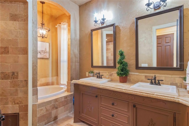 bathroom with a notable chandelier, a relaxing tiled tub, and vanity