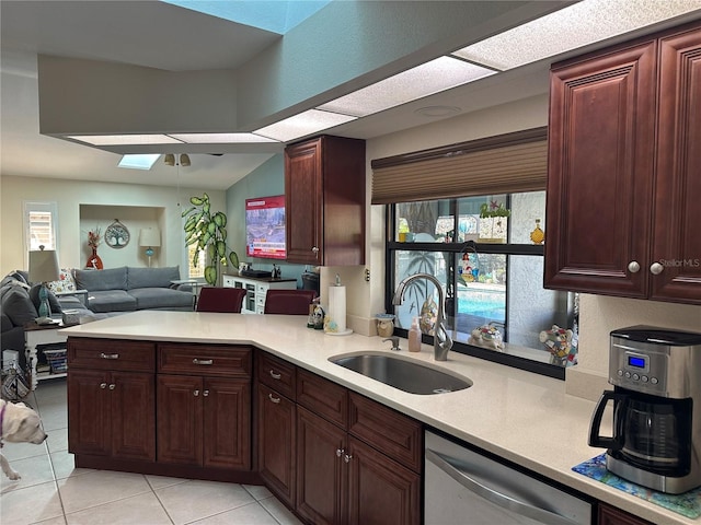 kitchen featuring vaulted ceiling with skylight, dishwasher, sink, light tile patterned floors, and kitchen peninsula