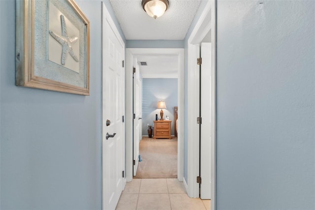 hall with light carpet and a textured ceiling