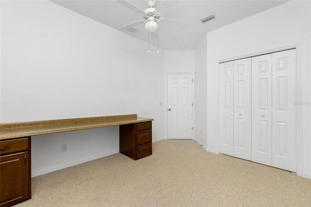 unfurnished office with ceiling fan, built in desk, and light carpet