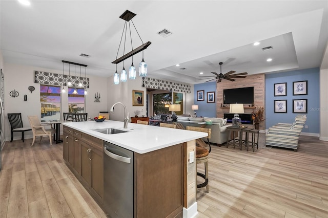 kitchen featuring stainless steel dishwasher, a raised ceiling, sink, and an island with sink