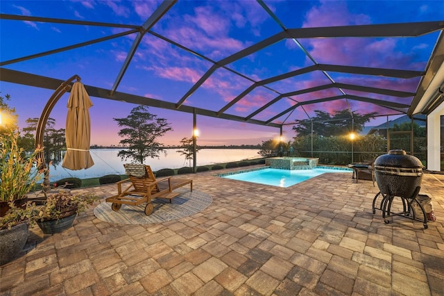 pool at dusk featuring glass enclosure, a water view, an in ground hot tub, and a patio