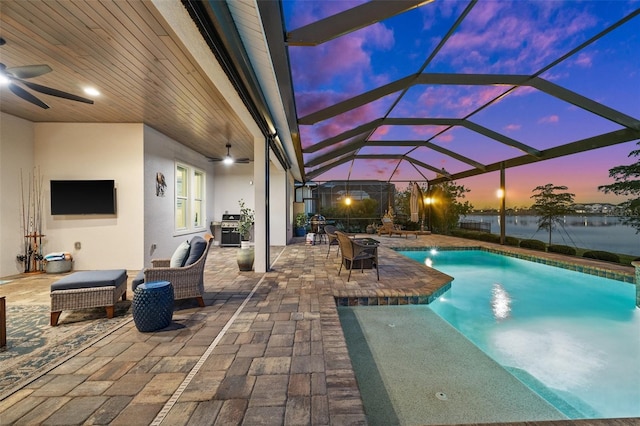 pool at dusk with pool water feature, ceiling fan, a lanai, a grill, and a patio