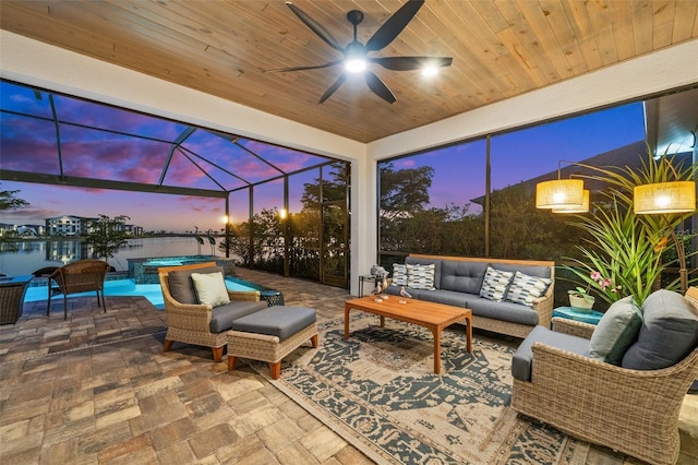 patio terrace at dusk featuring outdoor lounge area, ceiling fan, a pool with hot tub, a lanai, and a water view