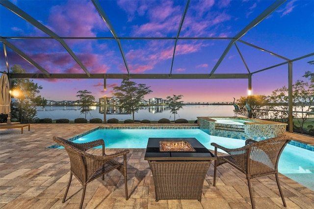 pool at dusk featuring an in ground hot tub, a water view, and a lanai