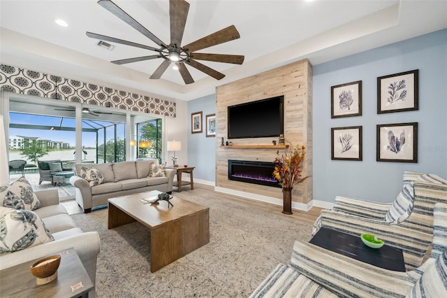 living room with a tile fireplace, light wood-type flooring, a raised ceiling, and ceiling fan