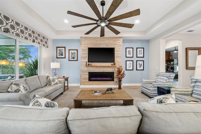 living room with hardwood / wood-style floors, ceiling fan, a tile fireplace, and a tray ceiling