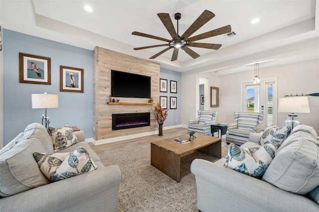 living room featuring a tray ceiling, ceiling fan, a fireplace, and light wood-type flooring