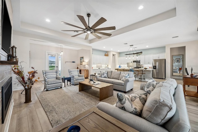 living room featuring ceiling fan, light hardwood / wood-style floors, and a raised ceiling