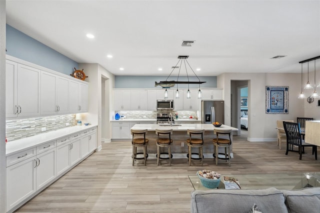 kitchen featuring decorative light fixtures, white cabinetry, a kitchen island with sink, and appliances with stainless steel finishes