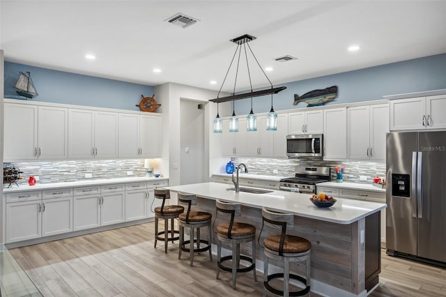 kitchen featuring pendant lighting, sink, an island with sink, appliances with stainless steel finishes, and white cabinetry