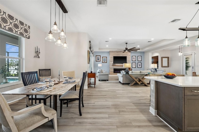 dining room featuring ceiling fan, a large fireplace, a raised ceiling, and light wood-type flooring