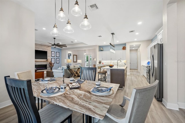 dining area with a fireplace, ceiling fan, sink, and light wood-type flooring