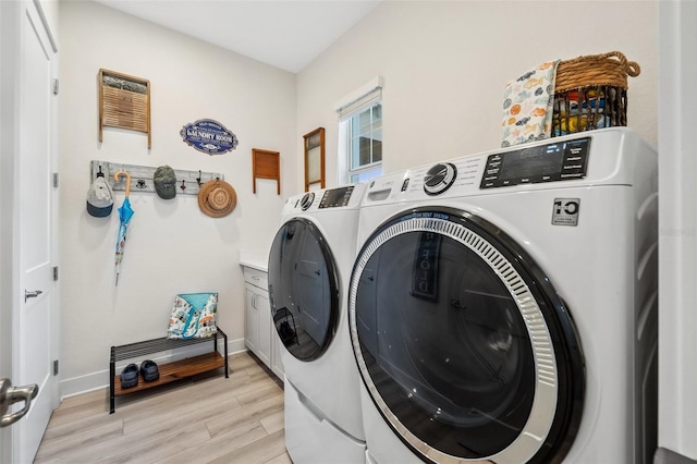 clothes washing area featuring cabinets, washing machine and dryer, and light hardwood / wood-style floors