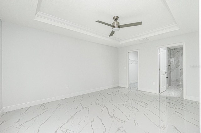 unfurnished bedroom featuring ceiling fan, a tray ceiling, and a walk in closet