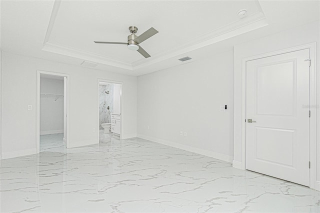 unfurnished bedroom with ceiling fan, a tray ceiling, ornamental molding, and ensuite bathroom