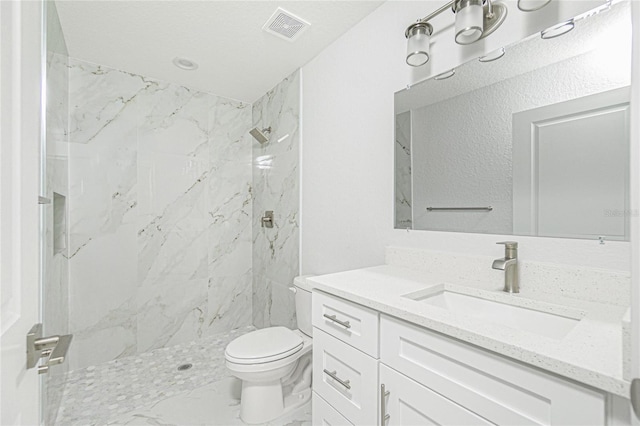 bathroom featuring toilet, tiled shower, and vanity