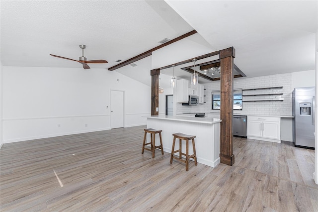 kitchen with lofted ceiling with beams, white cabinetry, hanging light fixtures, light hardwood / wood-style floors, and stainless steel appliances