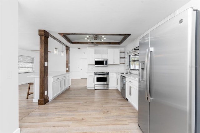 kitchen with sink, appliances with stainless steel finishes, a tray ceiling, pendant lighting, and white cabinets