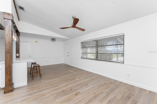 spare room featuring ceiling fan, lofted ceiling, light hardwood / wood-style floors, and a textured ceiling