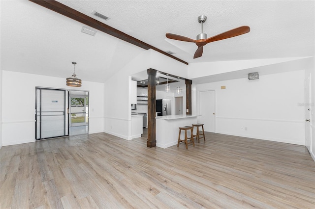 unfurnished living room with ceiling fan, vaulted ceiling with beams, a textured ceiling, and light hardwood / wood-style floors