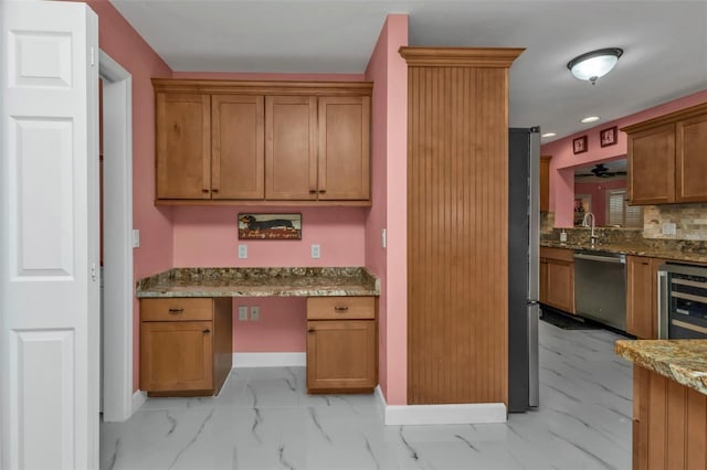 kitchen with light stone countertops, sink, beverage cooler, built in desk, and appliances with stainless steel finishes