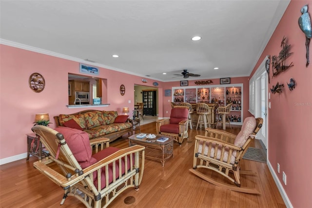 living room featuring ceiling fan, light hardwood / wood-style floors, crown molding, and bar area