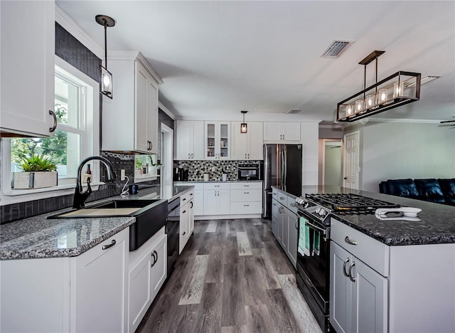 kitchen with dark stone counters, black appliances, sink, decorative light fixtures, and white cabinetry