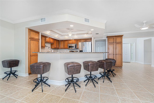 kitchen featuring ceiling fan, a raised ceiling, crown molding, appliances with stainless steel finishes, and a breakfast bar area