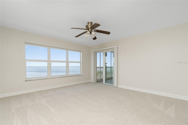 carpeted empty room featuring ceiling fan and a water view