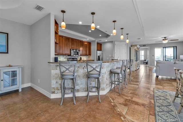 kitchen with pendant lighting, a breakfast bar, ceiling fan, appliances with stainless steel finishes, and kitchen peninsula