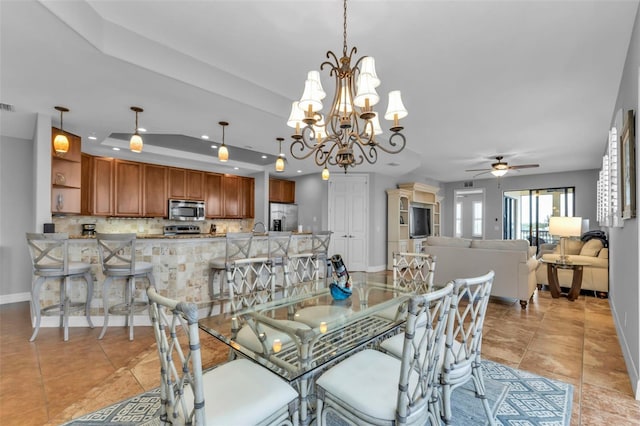 dining space with light tile patterned floors, ceiling fan with notable chandelier, and a tray ceiling