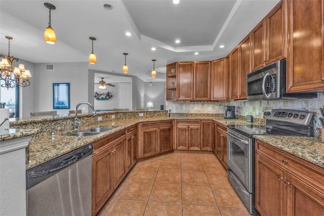 kitchen with appliances with stainless steel finishes, ceiling fan with notable chandelier, a raised ceiling, sink, and pendant lighting