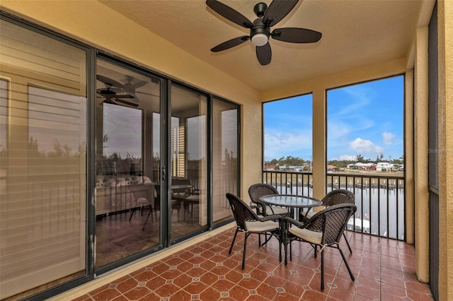 sunroom featuring ceiling fan and a water view