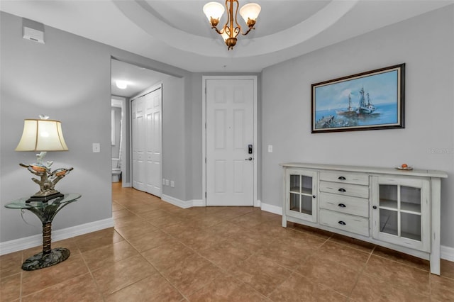 tiled entryway with a raised ceiling and an inviting chandelier