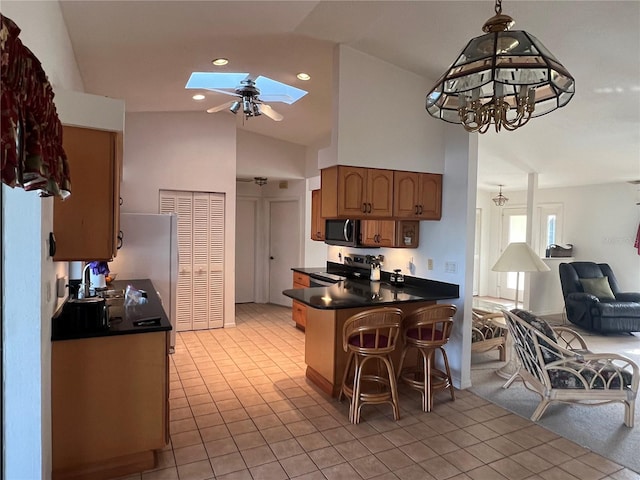 kitchen with decorative light fixtures, a skylight, stainless steel appliances, kitchen peninsula, and light tile patterned floors