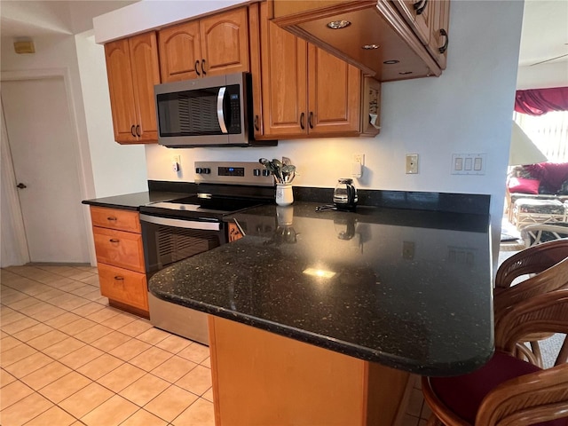 kitchen featuring light tile patterned flooring, stainless steel appliances, dark stone countertops, and kitchen peninsula