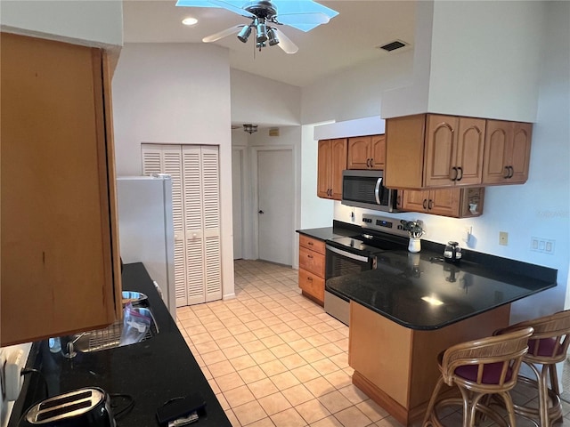 kitchen featuring ceiling fan, a breakfast bar, a skylight, stainless steel appliances, and light tile patterned floors