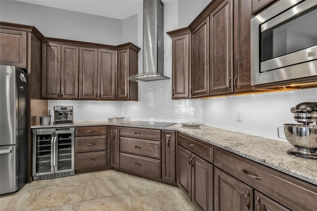 kitchen featuring dark brown cabinetry, appliances with stainless steel finishes, beverage cooler, light stone countertops, and wall chimney range hood