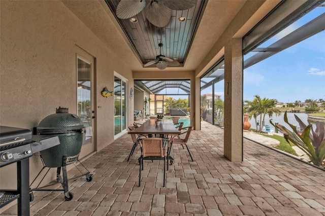 view of patio / terrace with grilling area, a water view, ceiling fan, and glass enclosure