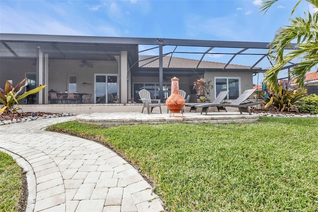 back of house featuring ceiling fan, a yard, a patio area, and glass enclosure