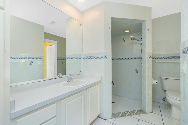 bathroom featuring toilet, a tile shower, tile patterned flooring, tile walls, and vanity