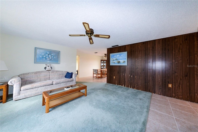 tiled living room with wooden walls, ceiling fan, and a textured ceiling