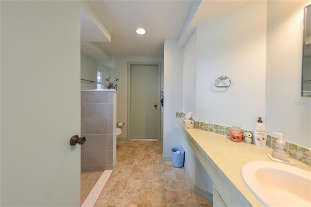 bathroom with tiled shower, vanity, and toilet