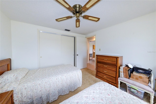 bedroom featuring a textured ceiling, light colored carpet, a closet, and ceiling fan