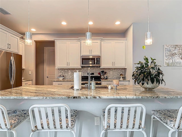 kitchen with white cabinetry, hanging light fixtures, tasteful backsplash, a breakfast bar, and appliances with stainless steel finishes